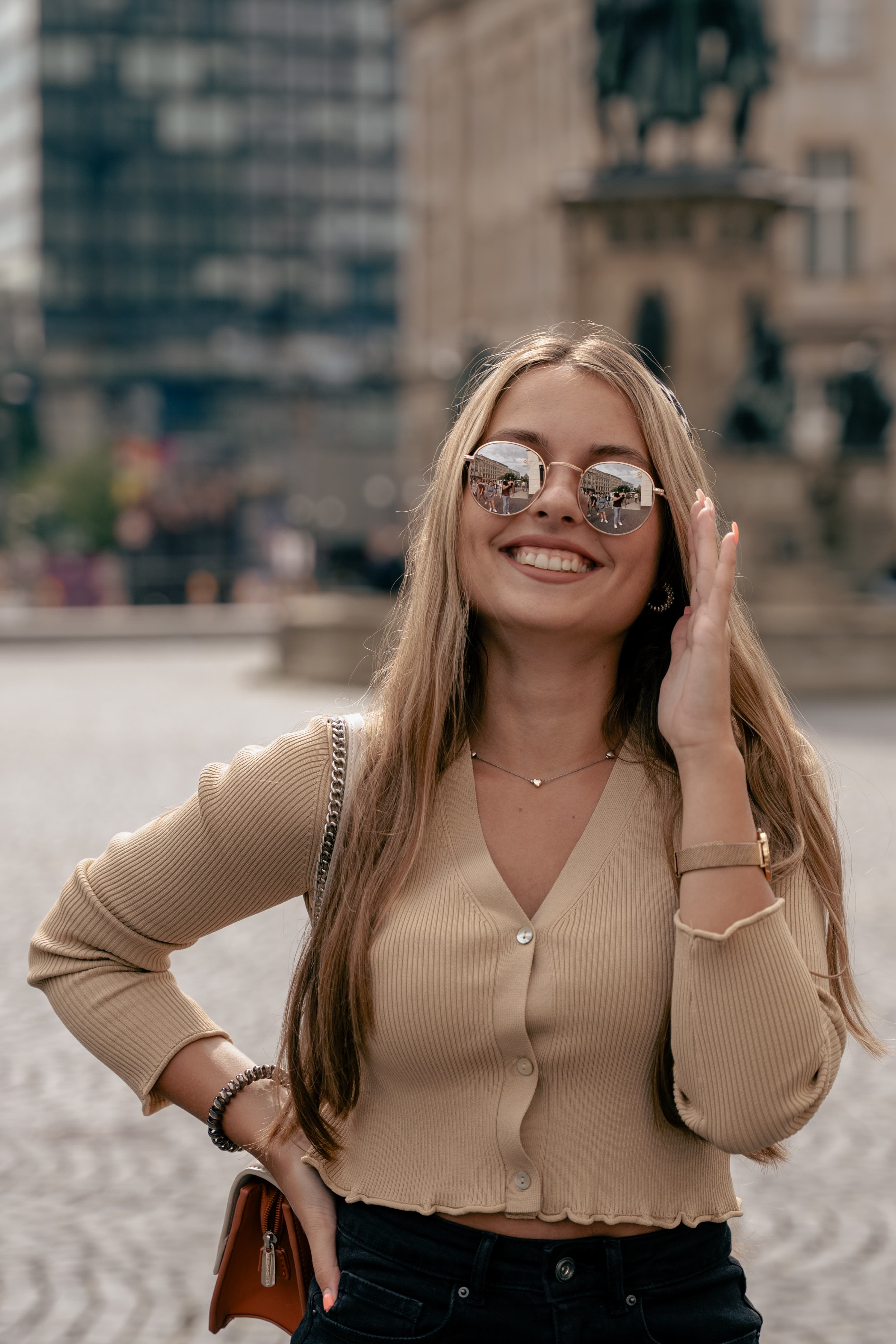 Lachende junge Frau mit runder Sonnenbrille, in deren Gläsern sich der Platz spiegelt